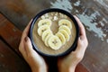 hands holding smoothie bowl, banana slices forming a heart on top