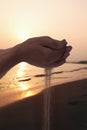 Hands holding and spilling sand with beach at sunset in the background Royalty Free Stock Photo