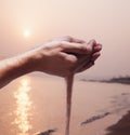 Hands holding and spilling sand with beach at sunset in the background Royalty Free Stock Photo