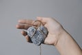 Hands holding a stone heart in jute bondage against grey background