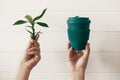 Hands holding stylish reusable eco coffee cup and green bamboo leaves on white wooden background. Zero waste. Green Cup from