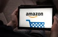 Hands holding tablet with Amazon shopping logo on a black screen.