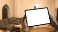 Hands holding tablet with blurred living room lighted with soft lights in background. Blank screen for your advertise