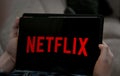 Hands holding tablet with Netflix logo on a black screen
