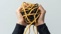 Hands Holding a Tangled Ball of Yellow and Black Cables in a Light Background for Creative Visual Concepts Royalty Free Stock Photo