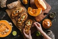 Hands holding toasted bread bruschetta with vegetable caviar, made of squash, pumpkin served with green pepper, nuts and lime on