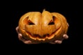 Hands holding a traditional Halloween creepy carved pumpkin Jack o lantern on black background. Happy Halloween