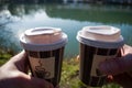 Hands holding two paper cups of coffee in the nature by the river Royalty Free Stock Photo