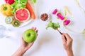 Hands holding a vegetable and apple with fruits, vegetables, dumbbell, tape measure and a glass of water on the white table Royalty Free Stock Photo