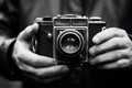 Hands holding vintage camera, black and white photo. Camera is made of metal and leather, with buttons and dials on it