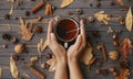 Hands holding warm cup of tea on background of autumn leaves, berries, nuts, anise, acorns, pine cones on rustic dark wood. Hello Royalty Free Stock Photo