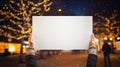 Hands holding a white blank paper in snowy city with christmas tree