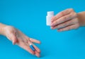 Hands holding white bottle for pills and pills on a blue background Royalty Free Stock Photo