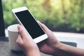 Hands holding white mobile phone with blank black desktop screen with coffee cup on table in cafe Royalty Free Stock Photo