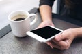 Hands holding white mobile phone with blank black desktop screen with coffee cup on table in cafe Royalty Free Stock Photo