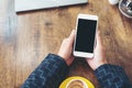 Hands holding white mobile phone with blank black desktop screen and coffee cup on wooden table in cafe background Royalty Free Stock Photo