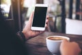 Hands holding white mobile phone with blank black desktop screen and a coffee cup on wooden table Royalty Free Stock Photo