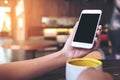 Hands holding white mobile phone with blank black desktop screen and a cup of coffee on wooden table in cafe Royalty Free Stock Photo