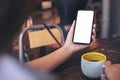 Hands holding white mobile phone with blank black desktop screen and a cup of coffee on wooden table in cafe Royalty Free Stock Photo