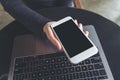 Hands holding white mobile phone with blank black desktop screen and laptop on table in cafe Royalty Free Stock Photo