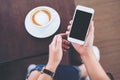 Hands holding white mobile phone with blank black screen with coffee cup on wooden table and floor background Royalty Free Stock Photo