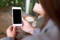 Hands holding white mobile phone with blank white screen with hot coffee cup on wooden table in cafe Royalty Free Stock Photo