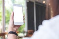 Hands holding white mobile phone with blank white screen in modern cafe Royalty Free Stock Photo