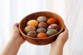 Hands holding wooden bowl with modern Easter eggs on white background. Stylish red, green and stone Easter eggs painted in natural Royalty Free Stock Photo