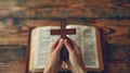 Hands holding a wooden cross over an open, aged Bible on a rustic wooden table, conveying a serene and spiritual mood. Royalty Free Stock Photo