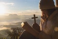 Hands holding wooden cross over open holy bible on the mountain background with morning sunrise, spirtuality and religion, Royalty Free Stock Photo