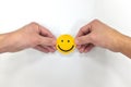 Hands holding a yellow smiley face on white background. Be positive and share happiness concept