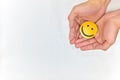 Hands holding a yellow smiling face on a white background. Be happy and share happiness concepts