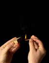 Hands holds a burning match on a black background. A wooden match burns in the hands of a macro. Igniting a match on a box. Smoke Royalty Free Stock Photo