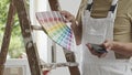 Hands of house painter man decorator choose the color using the sample swatch, work of the house to renovate, use mobile phone, a