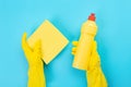 The hands of a housewife in yellow rubber protective gloves hold a bottle of household chemicals and a rag. Detergent for various