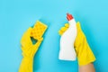 The hands of a housewife in yellow rubber protective gloves hold a bottle of household chemicals and a rag. Detergent for various