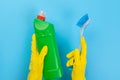 The hands of a housewife in yellow rubber protective gloves hold a bottle of household chemicals and a rag. Detergent for various