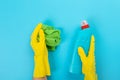 The hands of a housewife in yellow rubber protective gloves hold a bottle of household chemicals and a rag. Detergent for various