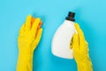 The hands of a housewife in yellow rubber protective gloves hold a bottle of household chemicals and a rag. Detergent for various