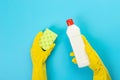 The hands of a housewife in yellow rubber protective gloves hold a bottle of household chemicals and a rag. Detergent for various