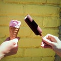 in hands ice cream in a waffle cone and chocolate popsicle on a yellow wall background Royalty Free Stock Photo