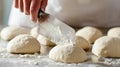 Hands of an individual using a metal dough scraper to portion balls of dough on a floured surface