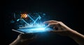 Hands interacting with a tablet, projecting digital graphs and data. The holographic