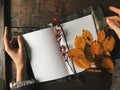 Hands keep notebook with white clean sheets on the wood table. Autumn leaves, warm colors, vintage texture. Copyspace background