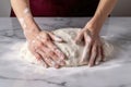 hands kneading raw pizza dough on a marble countertop