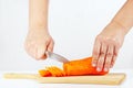Hands with a knife slices carrots on a cutting board