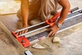 Hands of laborer using cutting tile machine at construction site with sun flare background