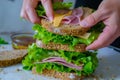 hands layering lettuce, ham, and cheese on whole grain bread