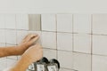 Hands laying modern square tile on adhesive close up. Worker installing stylish white tiles on plaster wall. Renovation