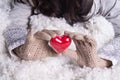 Hands in light teal knitted mittens are holding beautiful entwined vintage red heart in a snow.